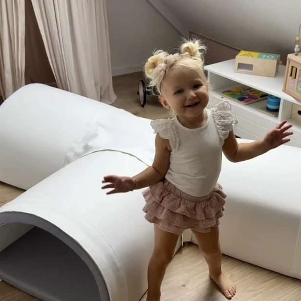 Dziecko raczkujące w miękkim tunelu z pianki w salonie
